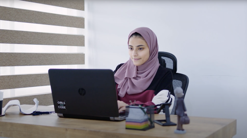 A woman wearing a hijab working on a laptop computer.